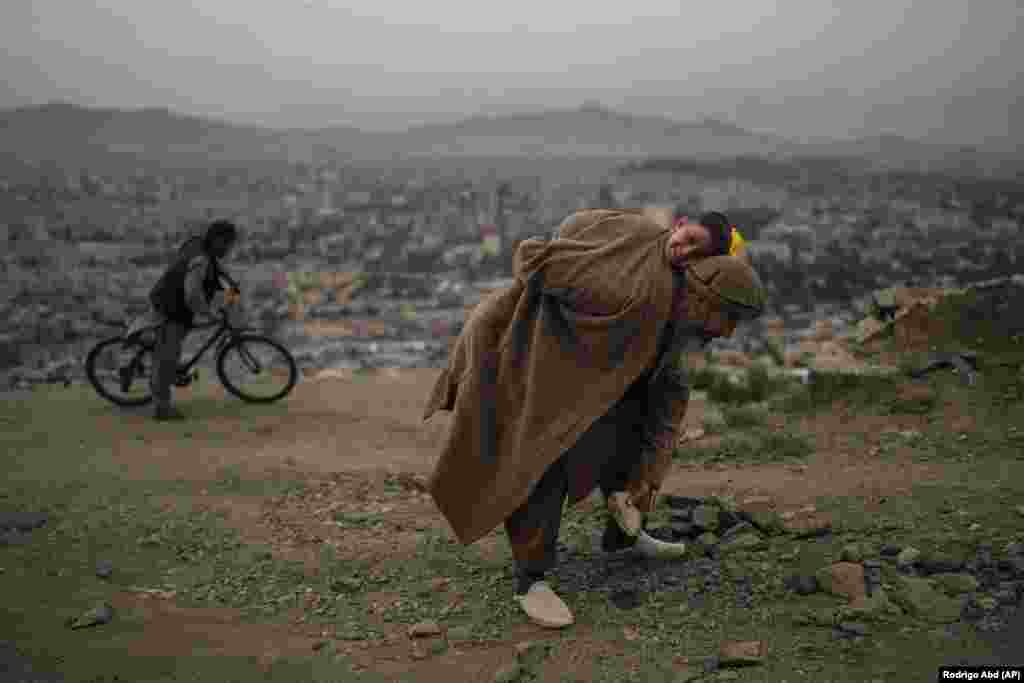 A man carrying his son removes stones from a road in Kabul so that bicycles and cars can travel better.&nbsp;