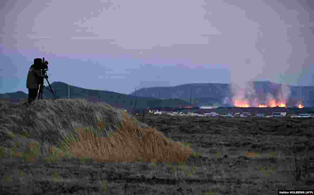 Një operator kamere duke qëndruar mbi një pirg për të xhiruar shpërthimet e lavës afër Grindavikut.