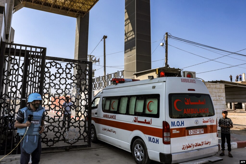 Një gazetar qëndron pranë ndërsa autoambulancat e Ministrisë palestineze të Shëndetësisë kalojnë portën për të hyrë në pikën kufitare Rafah më 1 nëntor 2023.