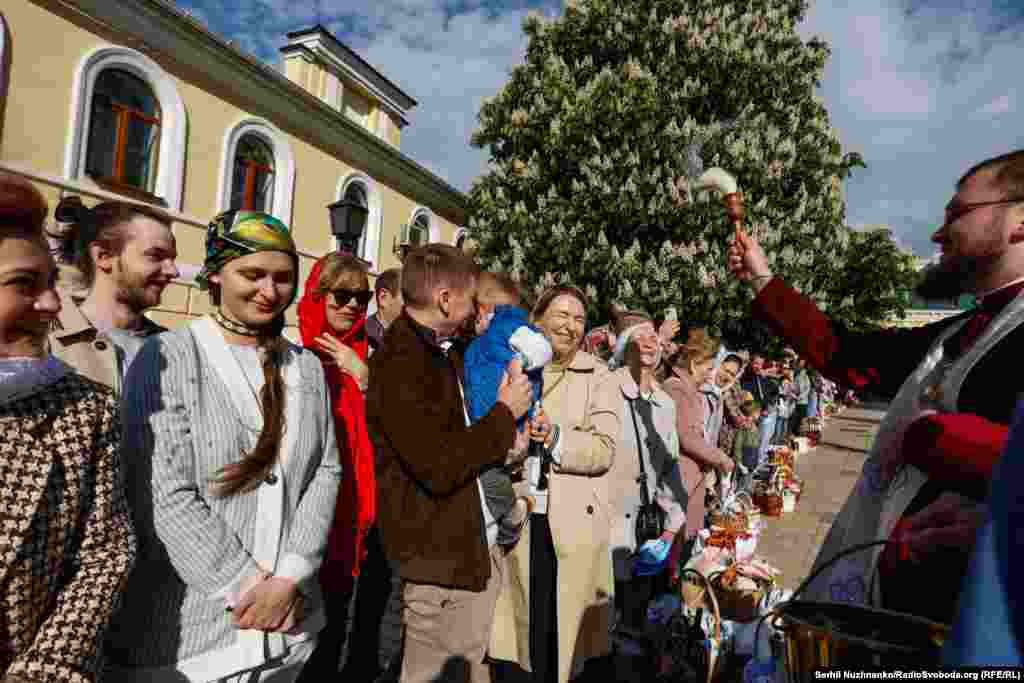 Священник щедро кропить освяченою водою кошики з великодніми стравами й вірян біля Михайлівського собору. Київ, 5 травня 2024 року