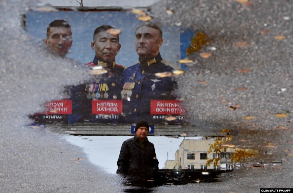 Një burrë kalon pranë një tabele që përshkruan portretet e oficerëve të ushtrisë ruse në Shën Petersburg, e cila është reflektuar në një pellg.