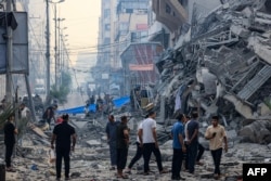 Жители идут по заваленной обломками улице перед зданием, рухнувшим во время авиаудара Израиля по городу Газа рано утром 8 октября 2023 года
