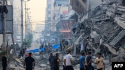 Жители одат по улица каде се урна зграда за време на израелски воздушен напад во градот Газа рано на 8 октомври 2023 година.