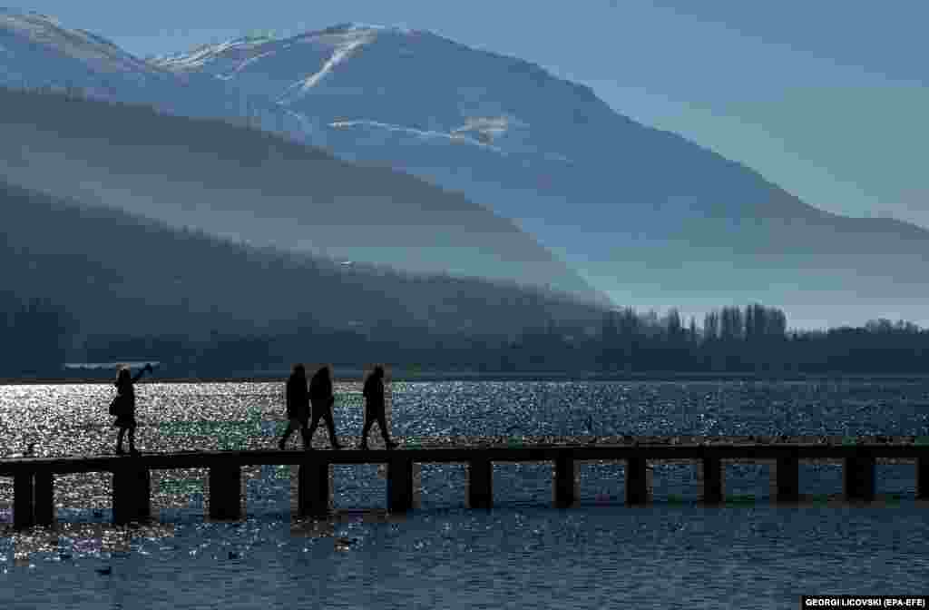 Ljudi u šetnji drvenim mostom po hladnom i sunčanom danu na Ohridskom jezeru u Severnoj Makedoniji.