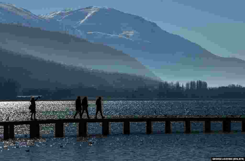 People walk over a wooden bridge on a cold and sunny day at Lake Ohrid in North Macedonia.&nbsp;