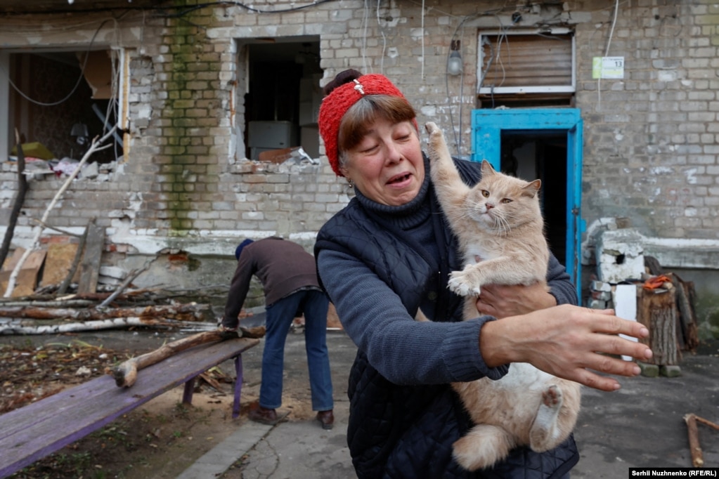 Një grua në qytetin Avdjiivka të Ukrainës mban një mace ndërsa fqinji i saj shkurton dru zjarri pranë ndërtesës së tyre të banimit, e cila është dëmtuar rëndë nga granatimet e vazhdueshme ruse.