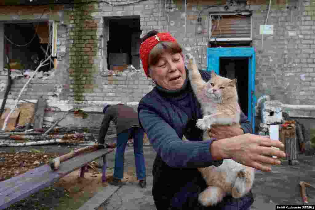 A woman in the Ukrainian frontline town of Avdiyivka holds a cat while her neighbor saws firewood next to their residential building, which has been heavily damaged by constant Russian shelling.