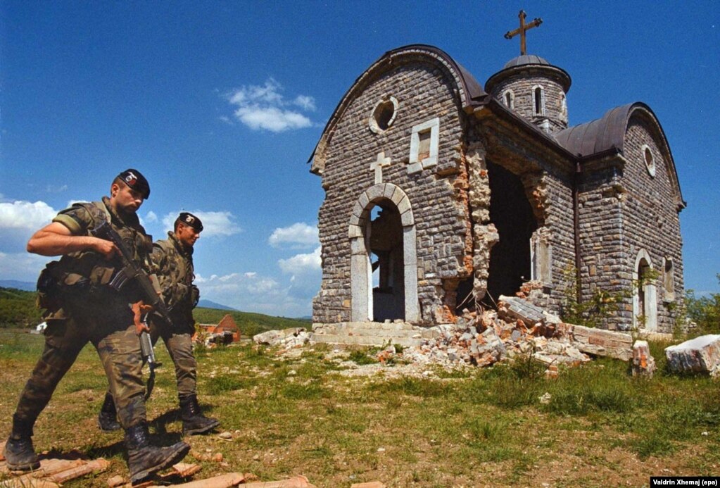Испански миротворци минават покрай повредена църква в Осоян, Косово, през май 2000 г.