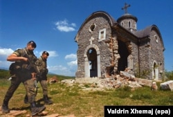 Las fuerzas de paz españolas pasan junto a una iglesia dañada en Osojan en mayo de 2000.