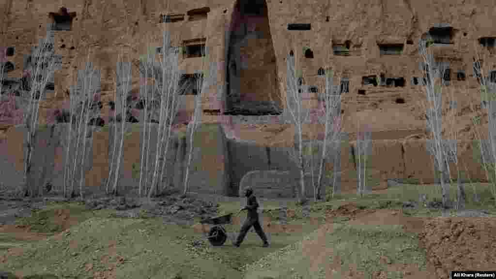 Un muncitor afgan împinge o roabă sub spațiul gol în care se afla cândva o statuie a lui Buda, veche de 1.400 de ani, în Bamiyan, Afganistan. Arheologii care lucrează pentru a conserva puținul patrimoniu cultural care mai există în Valea Bamiyan au avut de-a face cu săpături ilegale, cu dezvoltări imobiliare și cu pistolari talibani care folosesc rămășițele Buda pentru a se antrena la țintă.