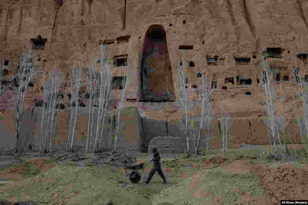 یک کارگر افغان با چرخ دستی اش در حال عبور از زیر فضای خالی که زمانی مجسمه بودا ۱۴۰۰ ساله در بامیان افغانستان قرار داشت. باستان شناسان تلاش دارند تا میراث های فرهنگی اندکی که هنوز در دره بامیان وجود دارد، حفظ گردند. &nbsp;