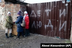 Дети у забора поврежденного дома в Мариуполе, оккупированном российскими войсками. 25 февраля 2023 года