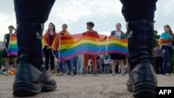 Policajci gledaju kako ljudi mašu zastavama duginih boja tokom gay pridea u Sankt Petersburgu 2017.