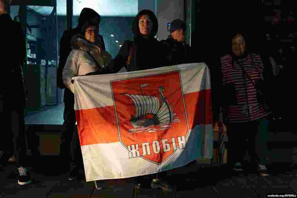 A Belarusian flag with the coat of arms and the name of the town of Zhlobin is displayed during the vigil. &nbsp;