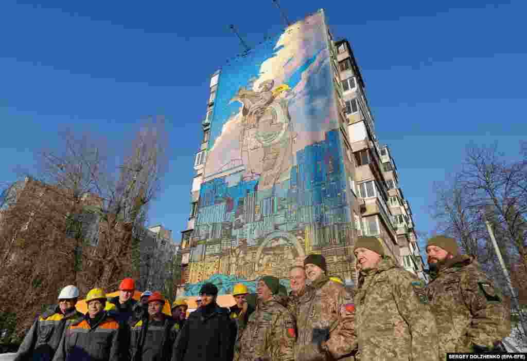 Ukrainian soldiers and energy workers stand in front of a mural dedicated to Ukrainian air defenses and energy workers in Kyiv.