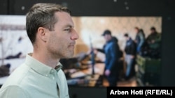 برندن هوفمن، عکاس خبری آمریکایی در حالی نمایشگاه را تماشا می‌کند که عکسی که او در روز دوم تهاجم گرفته است در پس زمینه دیده می‌شود.