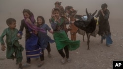 Afghan girls and women carry donated aid to their tents during a fierce sandstorm after the earthquake in Zendah Jan district in Herat Province in October 2023.
