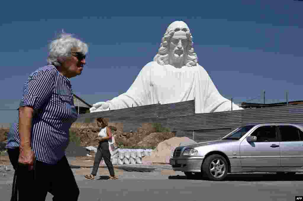 People pass by a giant sculpture of Jesus Christ by Armenian sculptor Armen Samvelyane, which will eventually have a height of 33 meters, at a workshop in Yerevan. The statue of Jesus Christ is to be erected on Mt. Hatis, some 30 kilometers from the Armenian capital.