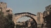 Ky imazh i marrë në gusht të vitit 1993 është një nga fotot e fundit të bëra nga Ura origjinale e Mostarit, e njohur në vend si &quot;Stari Most&quot;. Pavarësisht se ishte e mbështjellë me goma dhe e mbuluar me dërrasa druri, ura ra në lumin Neretva pas një breshëri sulmesh nga forcat etnike kroate në nëntor të vitit 1993.<br />
<br />
&nbsp;