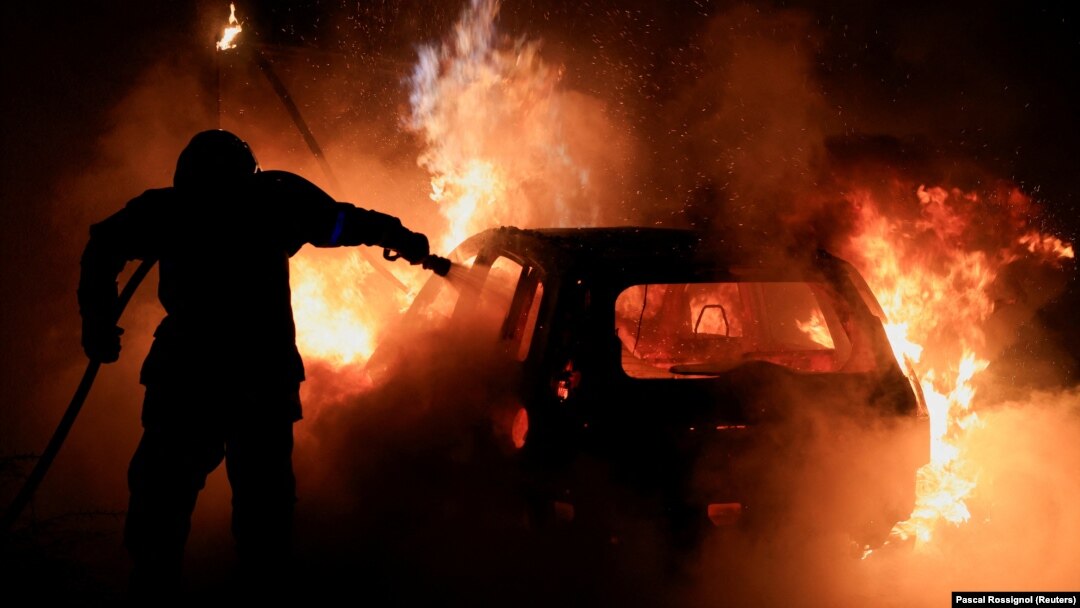 Un pompier francez încearcă să stingă o mașină în flăcări, în Tourcoing, pe 2 iulie 2023, în timpul celei de-a cincea zile de proteste după moartea lui Nahel, un adolescent de 17 ani ucis de un polițist francez în Nanterre în timpul unui control în trafic.