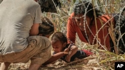 Бежанци, преминаващи в САЩ от Мексико, издърпват дете под телена мрежа по река Рио Гранде.