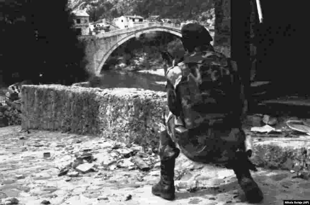 Egy szerb katona a mostari híd közelében 1992 júniusában. A híd túlélte az 1992&ndash;95-ös boszniai háború első szakaszát, amikor a szerbek a boszniai muszlim és horvát milíciák ellen harcoltak Mostar ellenőrzéséért. Amikor azonban a bosnyák muszlim és horvát szövetségesek egymás ellen fordultak, a híd stratégiai és szimbolikus célponttá vált a horvátok számára, akik az iszlám hódítás jelképének tekintették &nbsp;