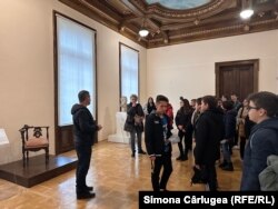 Un grup de elevi vizitează sala Brâncuși de la Muzeul de Artă din Craiova. Un muzeograf le prezintă operele marelui sculptor din patrimoniul muzeului.