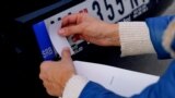 A man placing a sticker on a Serbian car plate to cover Serbian symbols. 