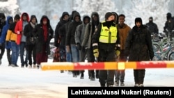 Finnish border guards escort migrants at the border crossing with Russia at Salla, northern Finland, on November 23.