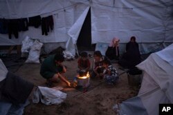 Palestinezët e zhvendosur në një kamp me tenda të siguruara nga UNDP-ja në Han Junis shihen duke zier ushqim në një zjarr në ambient të hapur.