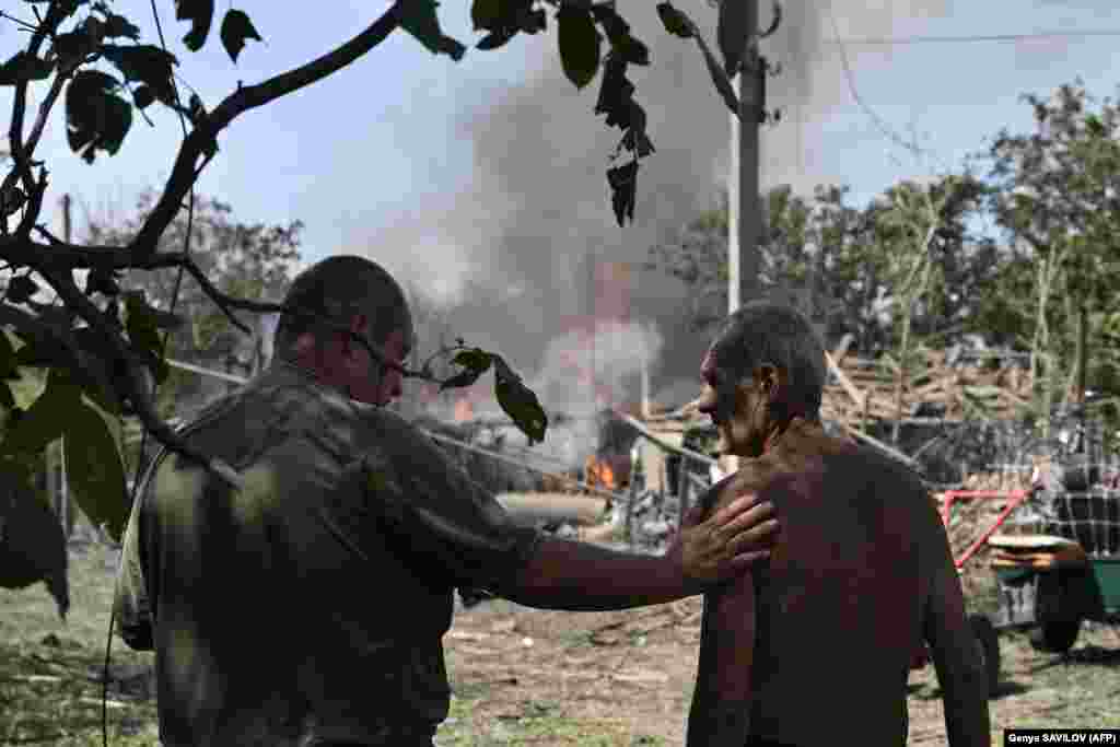  Local residents stand next to a burning house the day after a missile attack in Myrnograd, Donetsk region. &nbsp; 