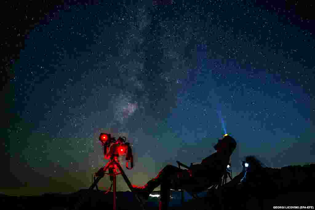 Astronom sedi pored kamera i posmatra zvezdano nebo očekujući da vidi i fotografiše kišu meteora Perseide iznad jezera Kozjak u Severnoj Makedoniji.