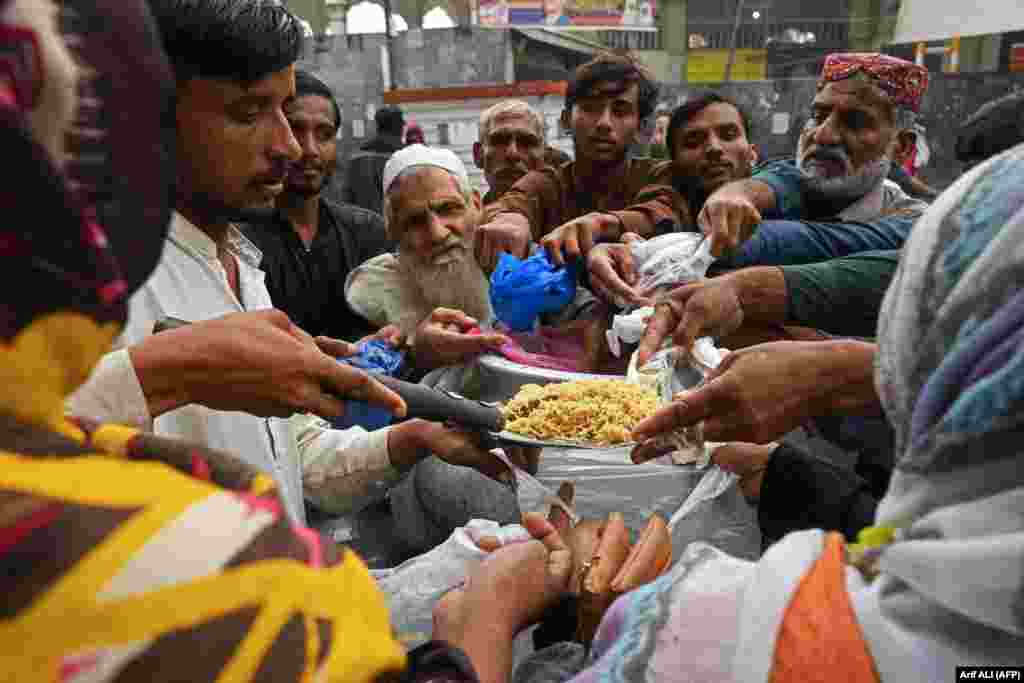 People gather along the roadside to receive free food being distributed on the occasion of World Food Day in Lahore, Pakistan.