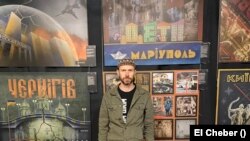 Рустем Скибін на тлі розроблених ним плакатів про міста України, які зазнали окупації. Фото El Cheber