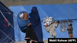 له پاکستانه افغانستان ته ستانه کړای شوي افغان کډوال. په عکس کې لیدل کېږي چې یوه مېرمن خپلې خیمې ته توکي لېږدوي.