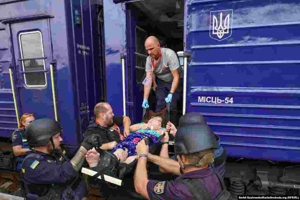 The distant sound of artillery fire intensifies the sense of urgency as an elderly woman is loaded onto the evacuation train.