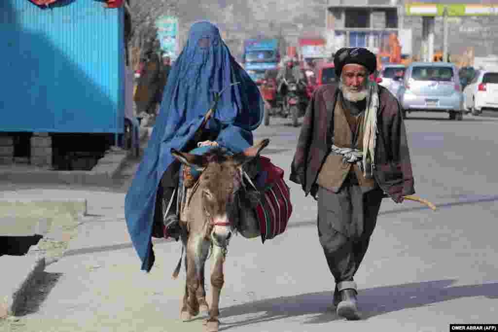A man walks beside a burqa-clad woman riding a donkey along a street in Fayzabad, Afghanistan.&nbsp;