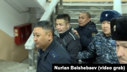 Azamat Estebesov (second from left) is accompanied by police at a court in Sokuluk on January 26. 