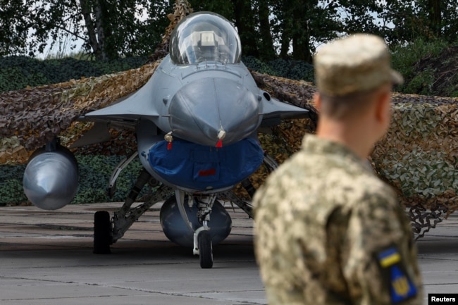 Український військовослужбовець стоїть поряд з одним із перших винищувачів F-16, наданих союзниками України, 4 серпня 2024 року