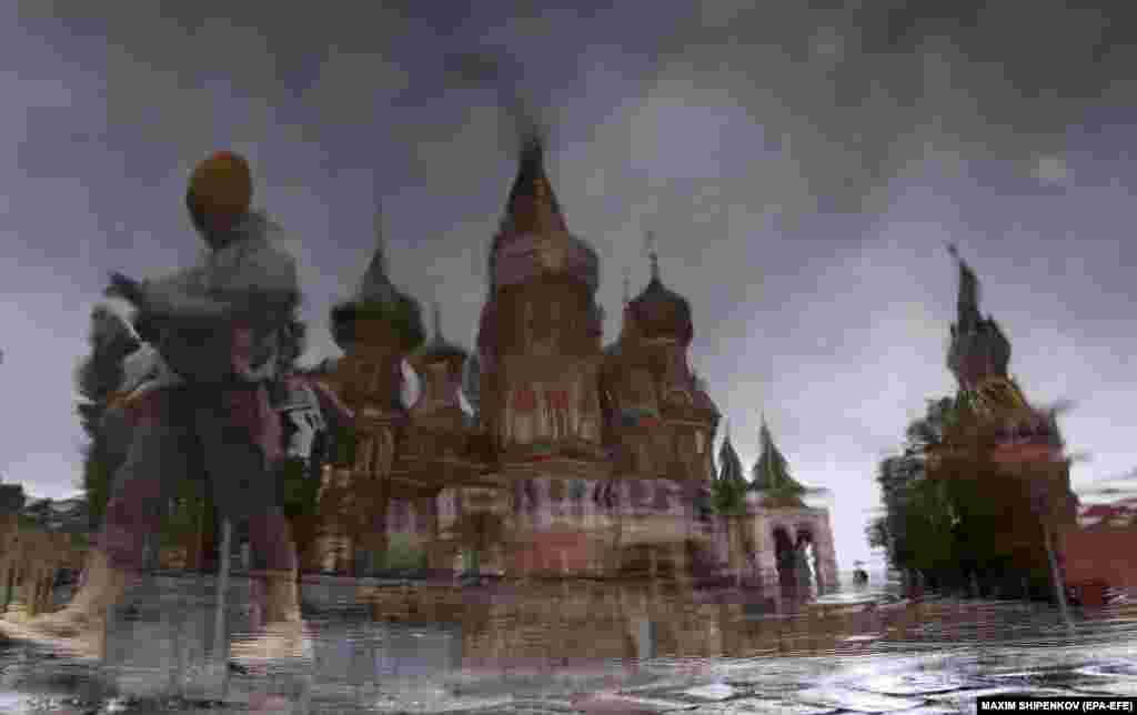 An image rotated 180 degrees shows a person walking near St. Basil&#39;s Cathedral and the Moscow Kremlin reflected in a puddle on a rainy day in downtown Moscow.