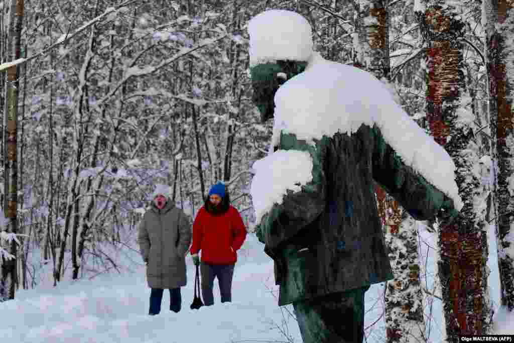 People walk past a snow-covered bronze monument depicting Soviet state founder Vladimir Lenin in a park near St. Petersburg.