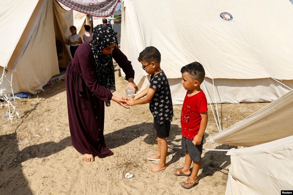 Një grua lan duart e një fëmije, ndërsa palestinezët, të cilët u larguan nga shtëpitë e tyre mes sulmeve izraelite, strehohen në kampin me tenda në një qendër të drejtuar nga Kombet e Bashkuara në Han Junis në Rripin e Gazës, më 23 tetor 2023.