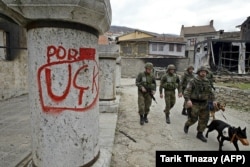 Pasukan KFOR melewati Katedral St. George di Prizren pada bulan Maret 2004 setelah mengalami kerusakan parah. Grafiti tersebut menunjukkan dukungan terhadap Tentara Pembebasan Kosovo (UCK).