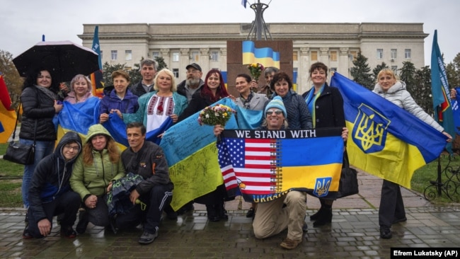 Le persone tengono le bandiere nazionali e posano per una foto mentre la città celebra un anno da quando l'Ucraina ha ripreso la città di Kherson dalle forze di occupazione russe, nel centro di Kherson, l'11 novembre.