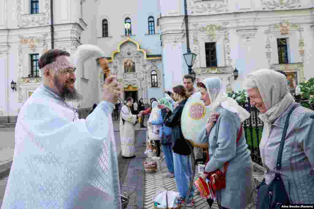 Një prift shpërkatë me ujin e shenjtë besimtarët gjatë shërbesës për pashkët në Manastirin Peçersk Lavra në Kiev më 5 maj 2024. Kisha Ortodokse e Ukrainës u nda nga ajo ruse më 2019.&nbsp;
