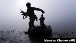 Український військовослужбовець вистрибує з човна біля берега Дніпра на Херсонщині, 15 жовтня 2023 року