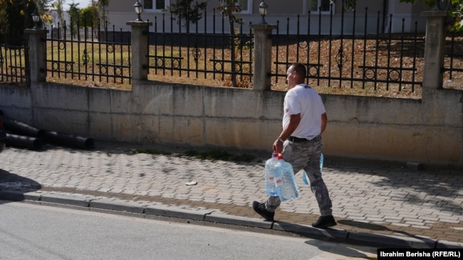 Një qytetar duke bartur bidonë me ujë.