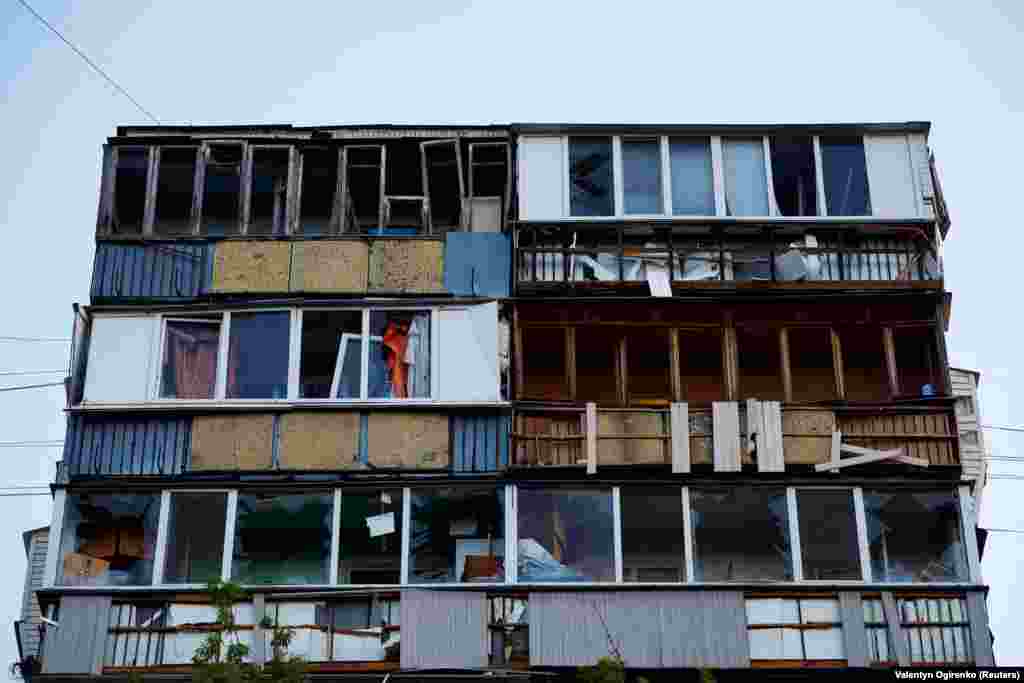 A view of the apartment building shows shattered windows and the damaged facade.