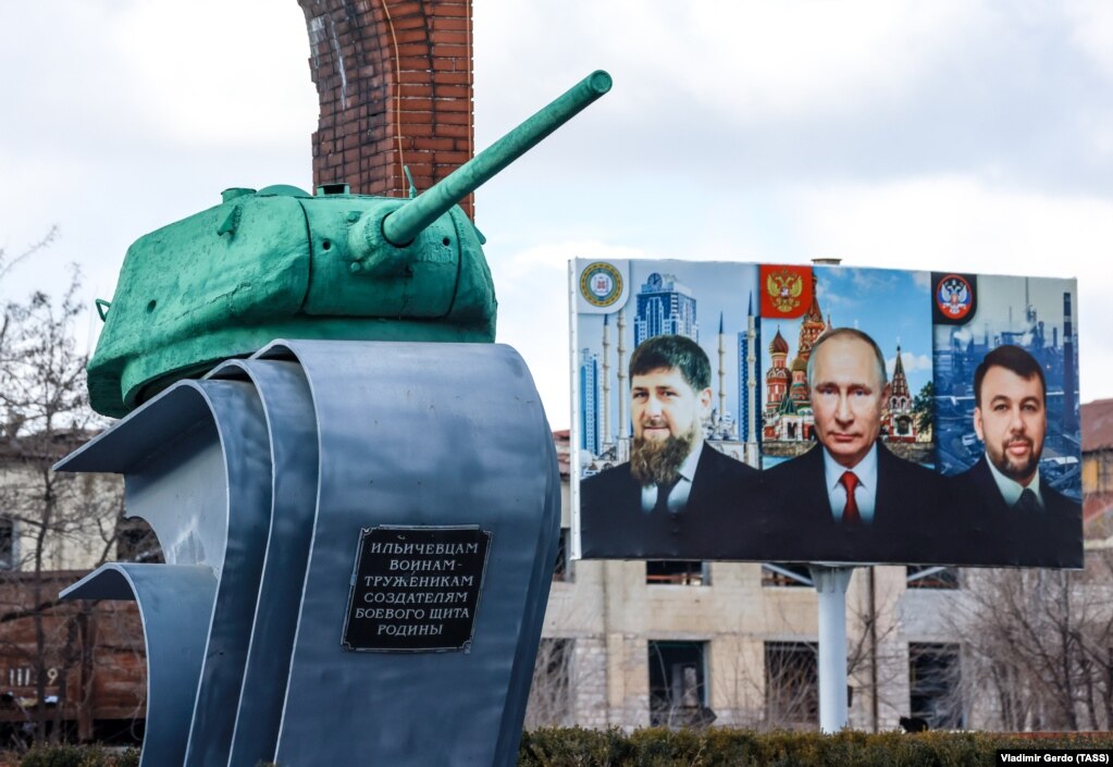 Një pano e udhëheqësit çeçen, Ramzan Kadyrov (majtas), presidentit rus, Vladimir Putin (në mes) dhe administratorit të pjesëve të kontrolluara nga Rusia të rajonit të Donjeckut,&nbsp;Denis Pushilin. Panoja gjendet&nbsp;përpara një memoriali në Mariupol, ndërsa fotografia u bë më 16 shkurt, 2023. Një raport i OKB-së vlerësoi se rreth 350.000 njerëz u detyruan të largohen nga Mariupoli. Qyteti kishte rreth 450.000 banorë para luftës.