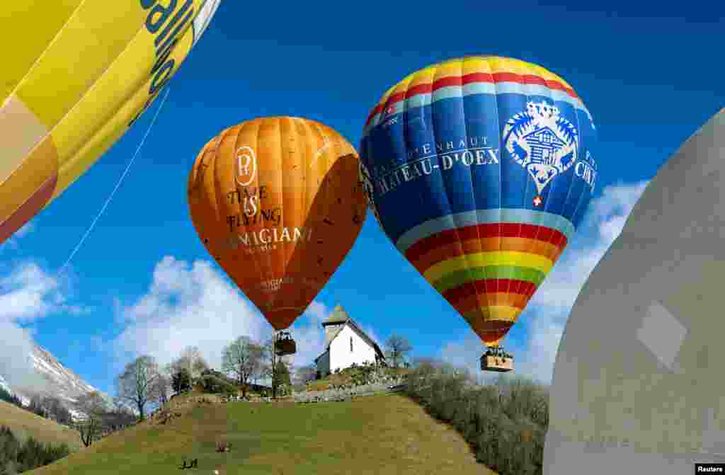 Disa balona shumëngjyrëshe duke u ngritur mbi një peizazh fshati. Balonat lëvizin në drejtim të rrymës së erës.&nbsp;&nbsp;